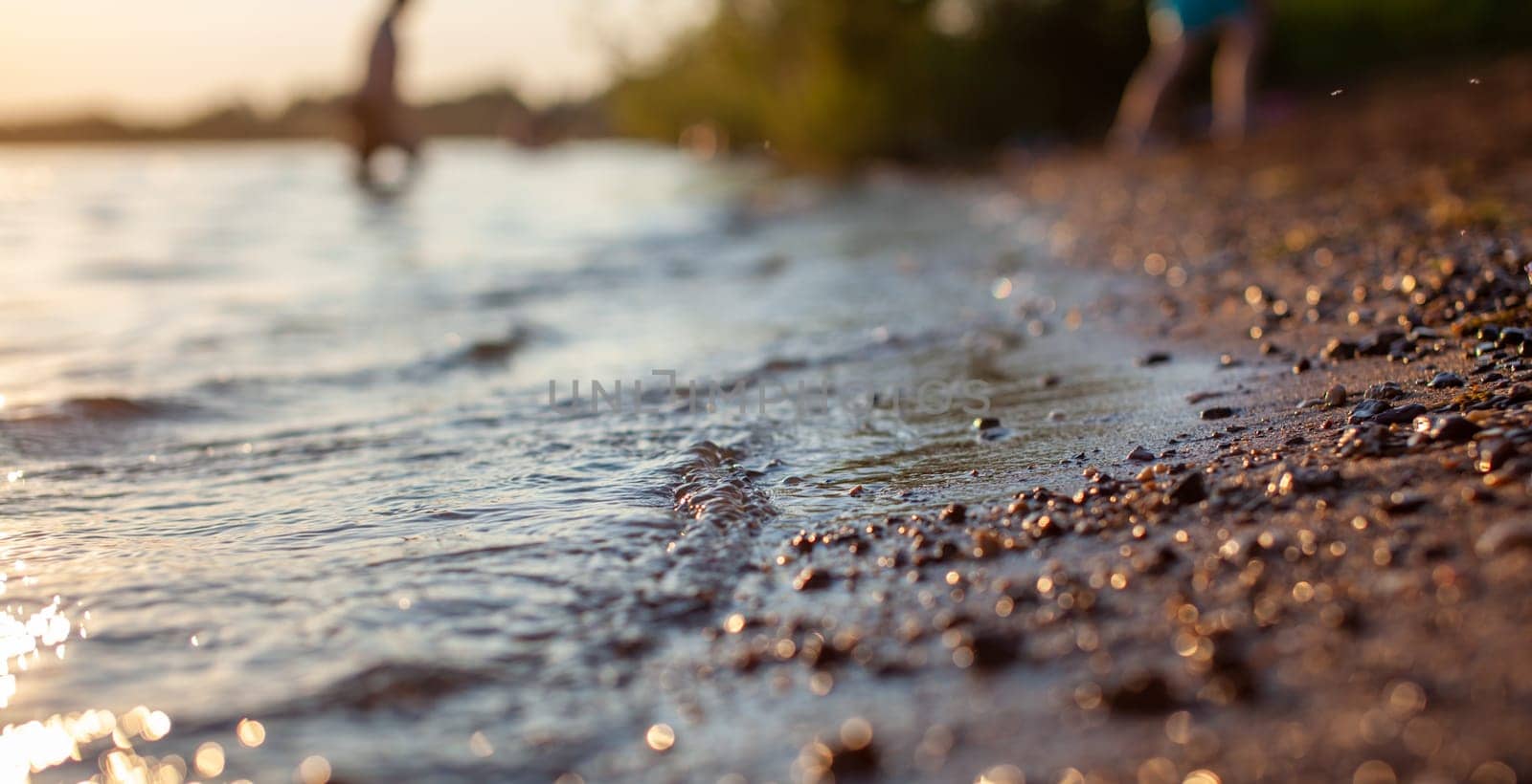 Close-up of the shore of a lake or river made of small stones against a colorful sunset background. A beautiful place in nature for family holidays and swimming.
