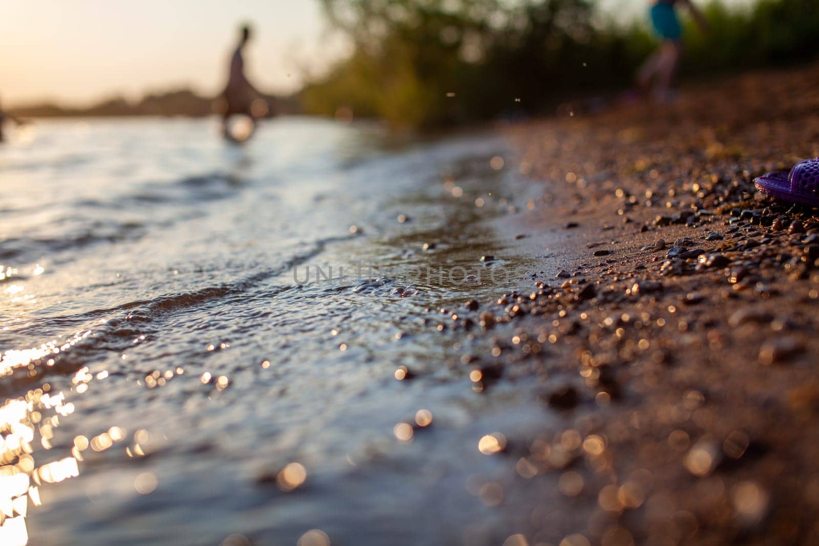 Close-up of the shore of a lake or river made of small stones against a colorful sunset background. A beautiful place in nature for family holidays and swimming.