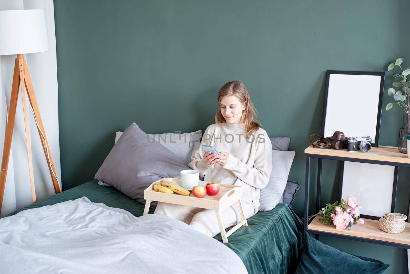 caucasian woman waking up in her bed in the morning. young millennial woman sitting on the bed in the morning drinking coffee, light and airy room