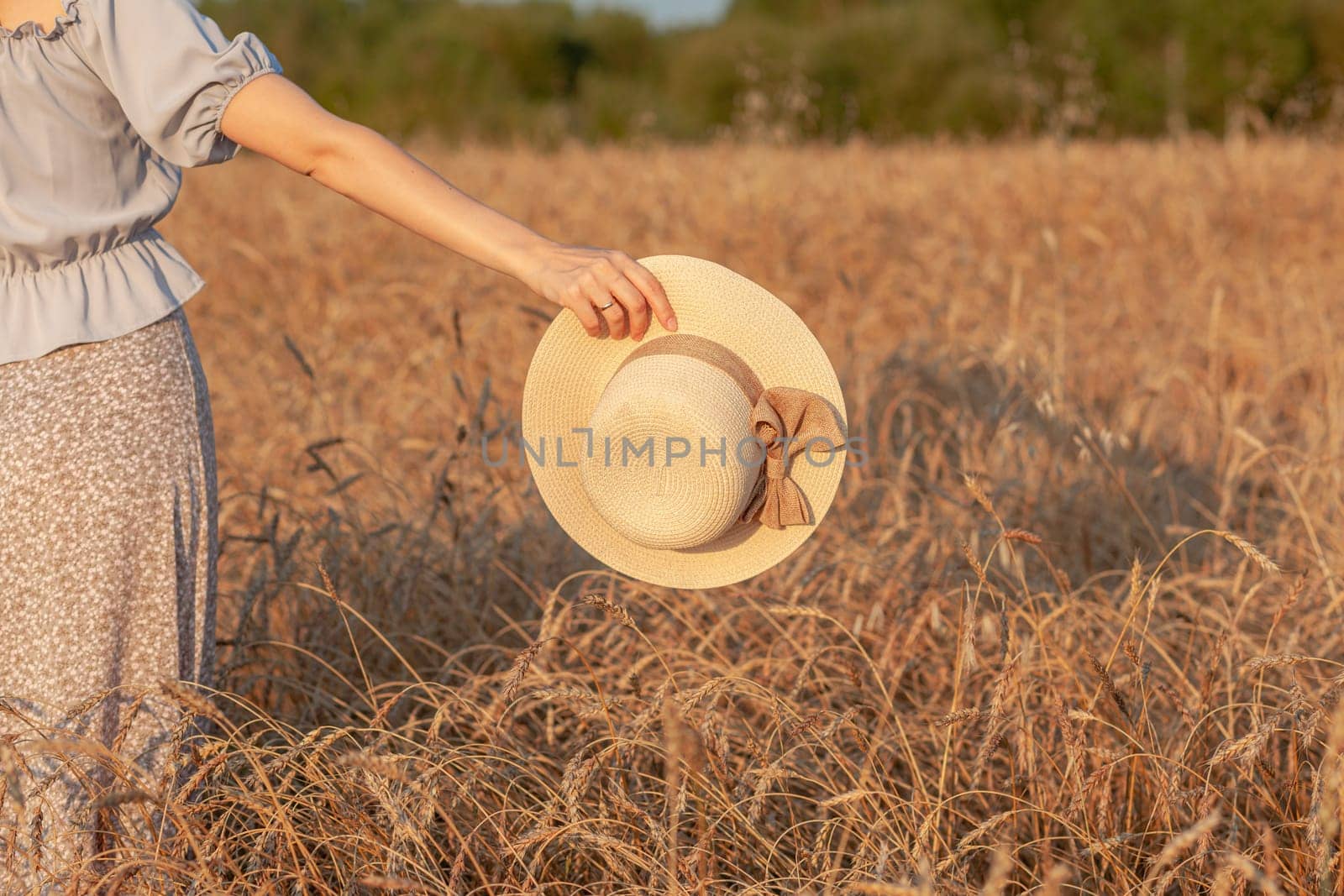 A girl holds a hat in her hand against the background of a wheat field by AnatoliiFoto
