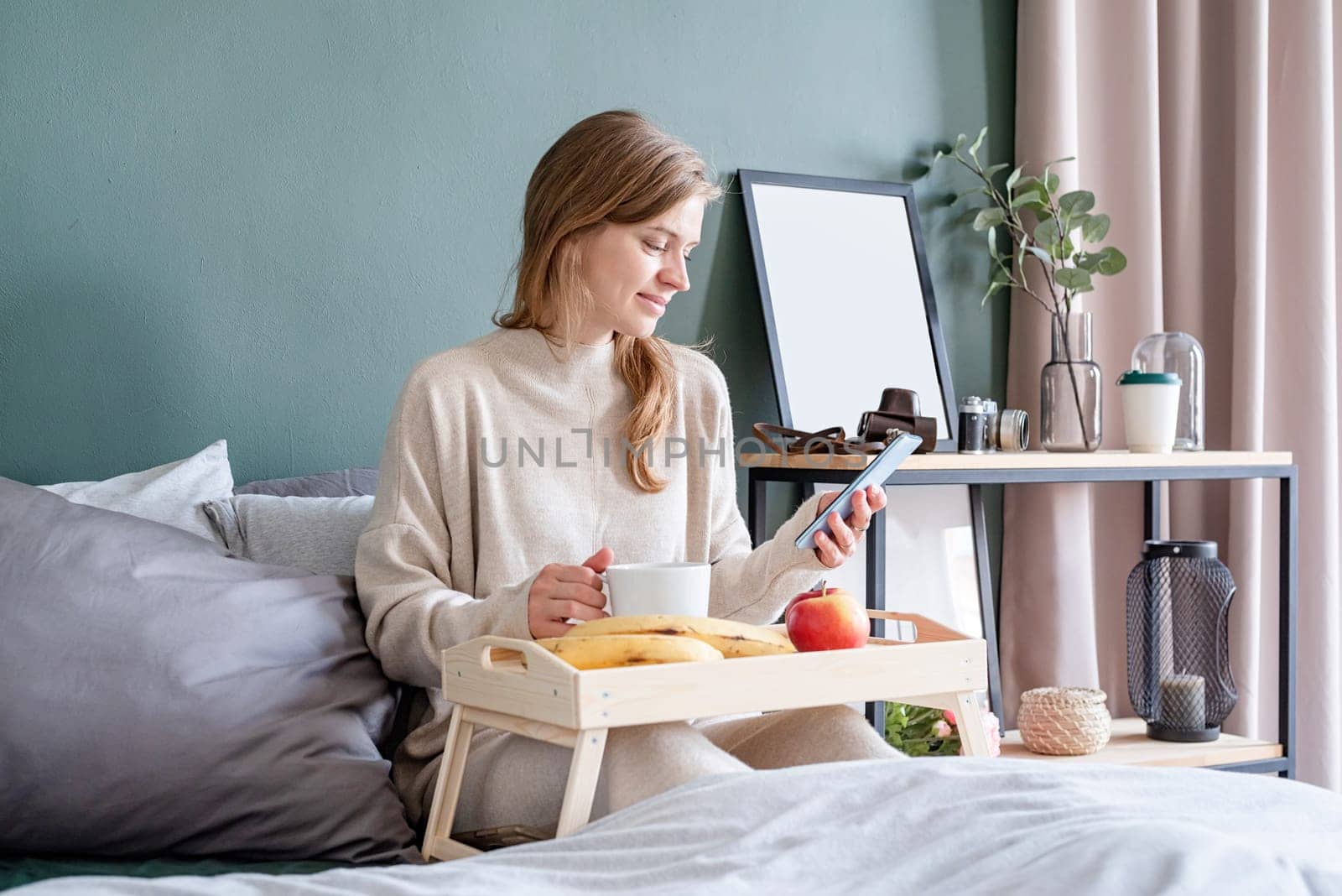 caucasian woman waking up in her bed in the morning. young millennial woman sitting on the bed in the morning drinking coffee, light and airy room