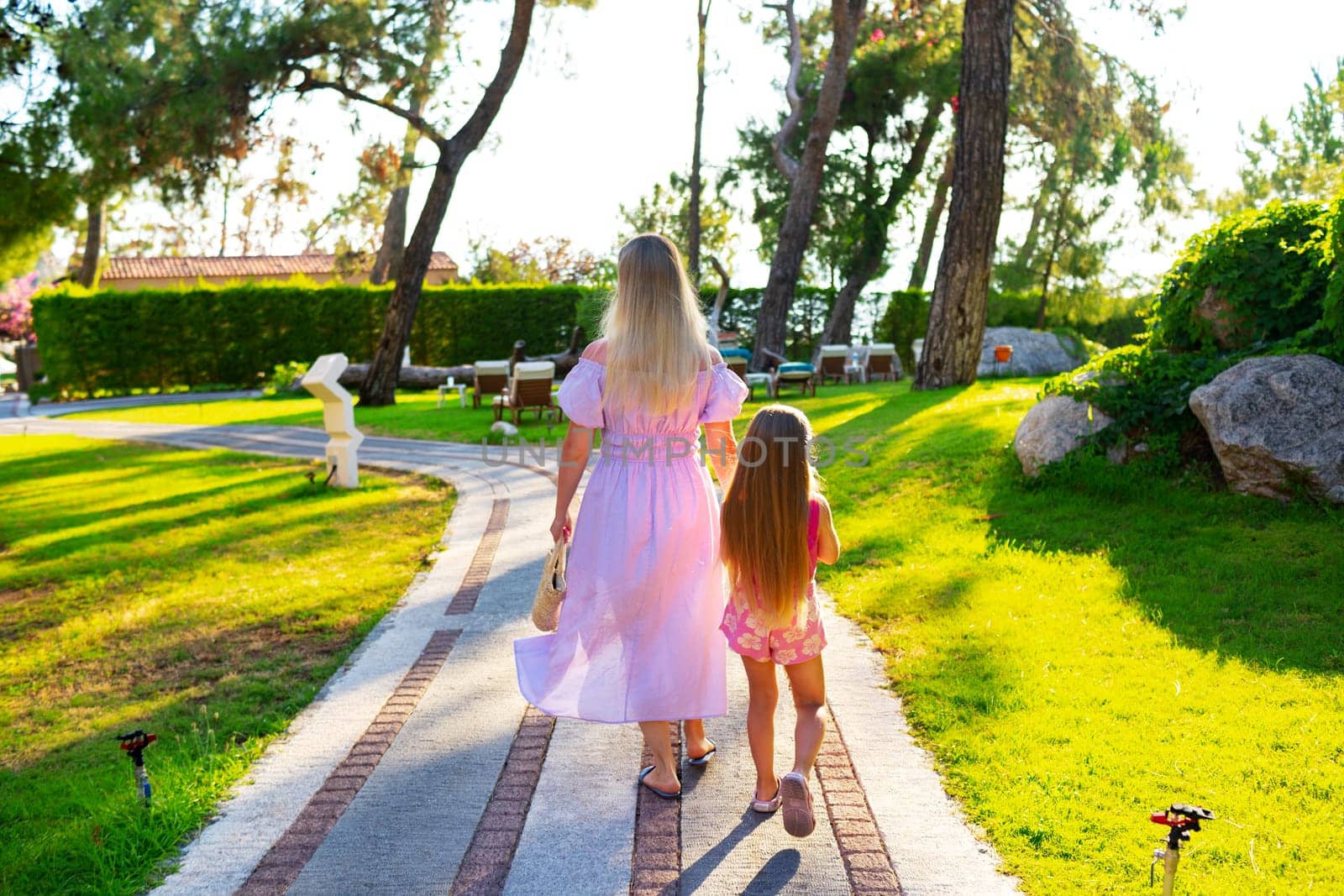 Mother and daughter enjoying walk outdoors in summer, back view