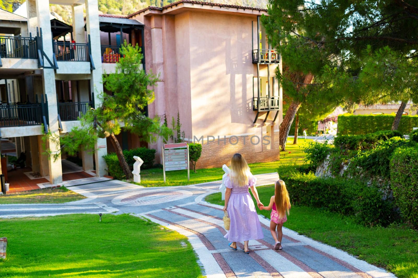 Mother and daughter enjoying walk outdoors in summer, back view