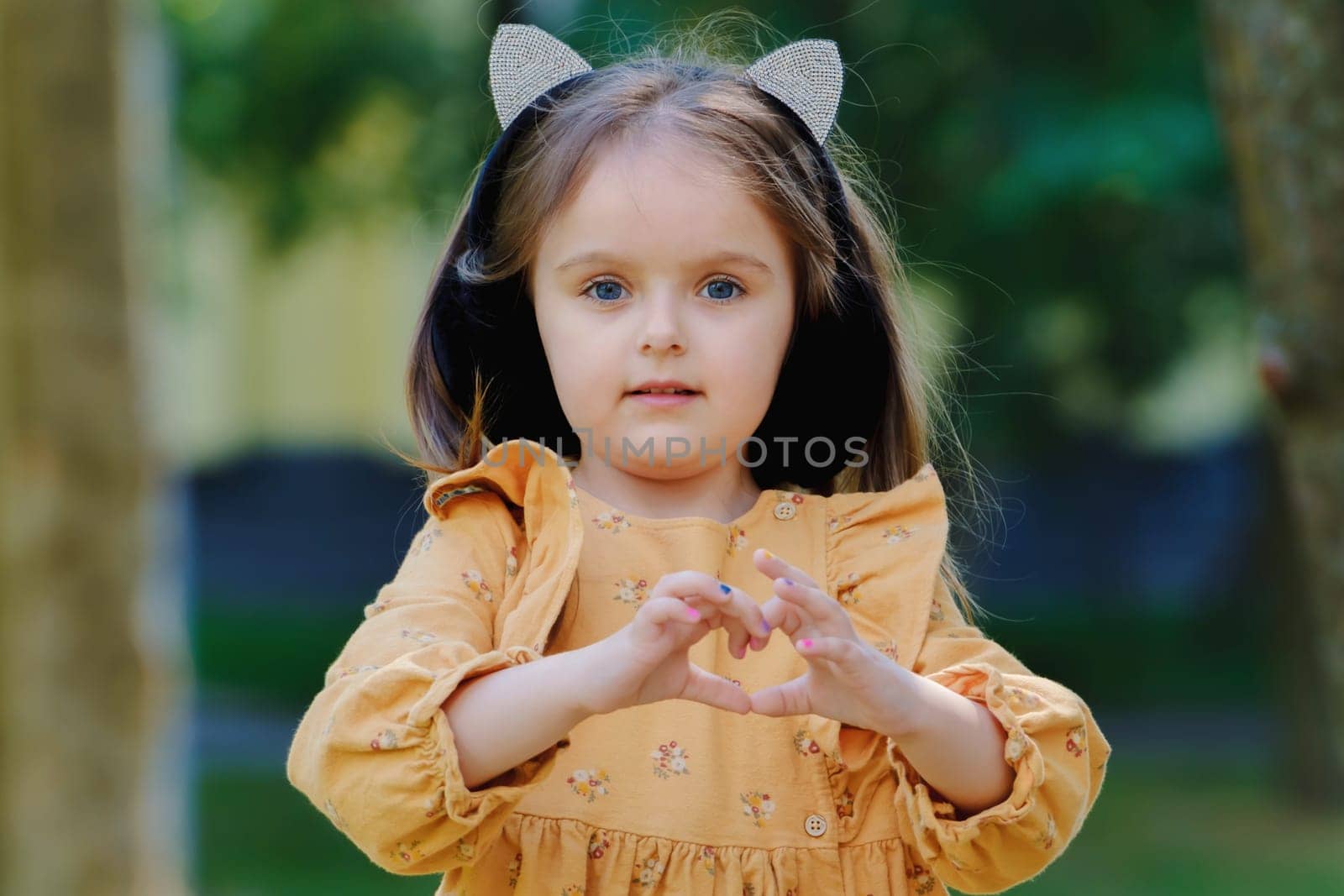 Portrait of a cute little girl in the park and shows a heart sign with her hands.