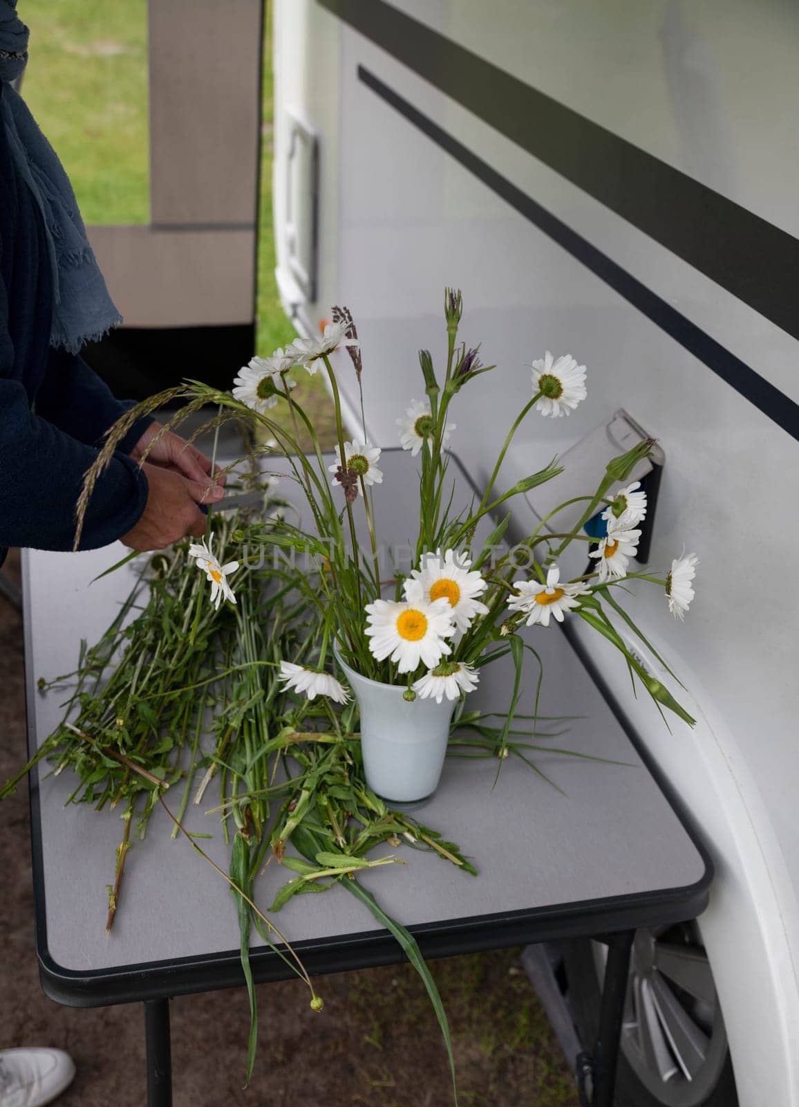 a woman is outside the caravan making a bouquet of wildflowers such as daisies