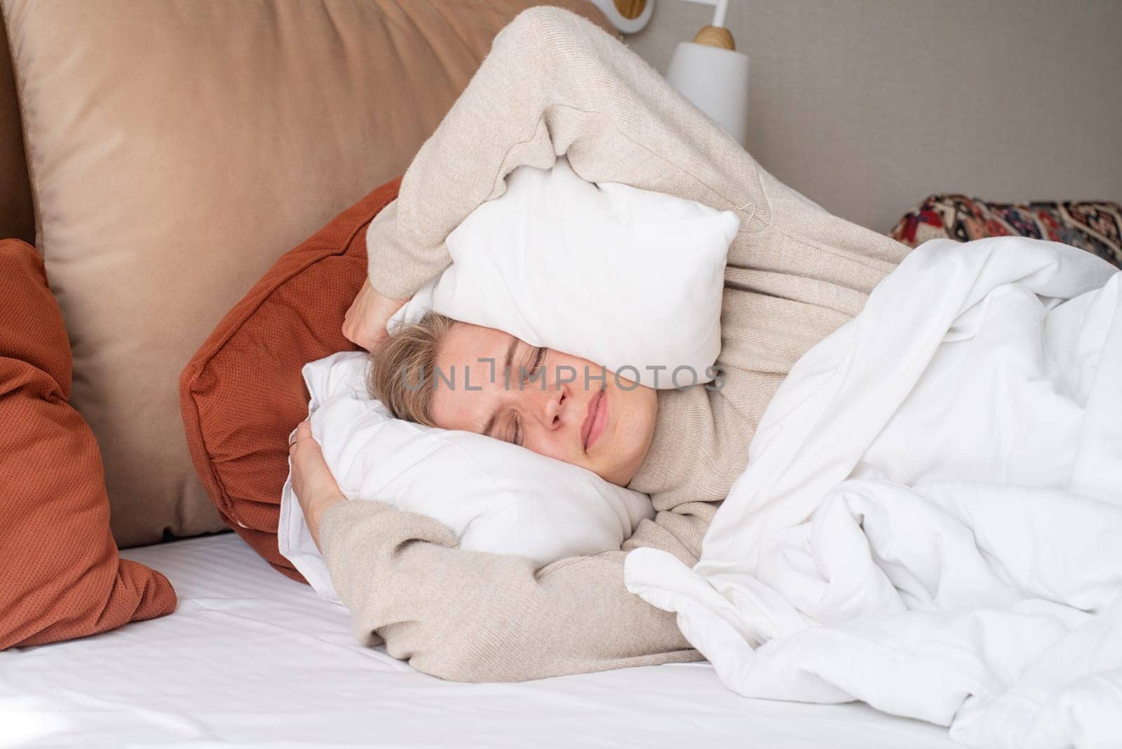 Woman sleeping at bed at home, covering ears with pillows from noise by Desperada