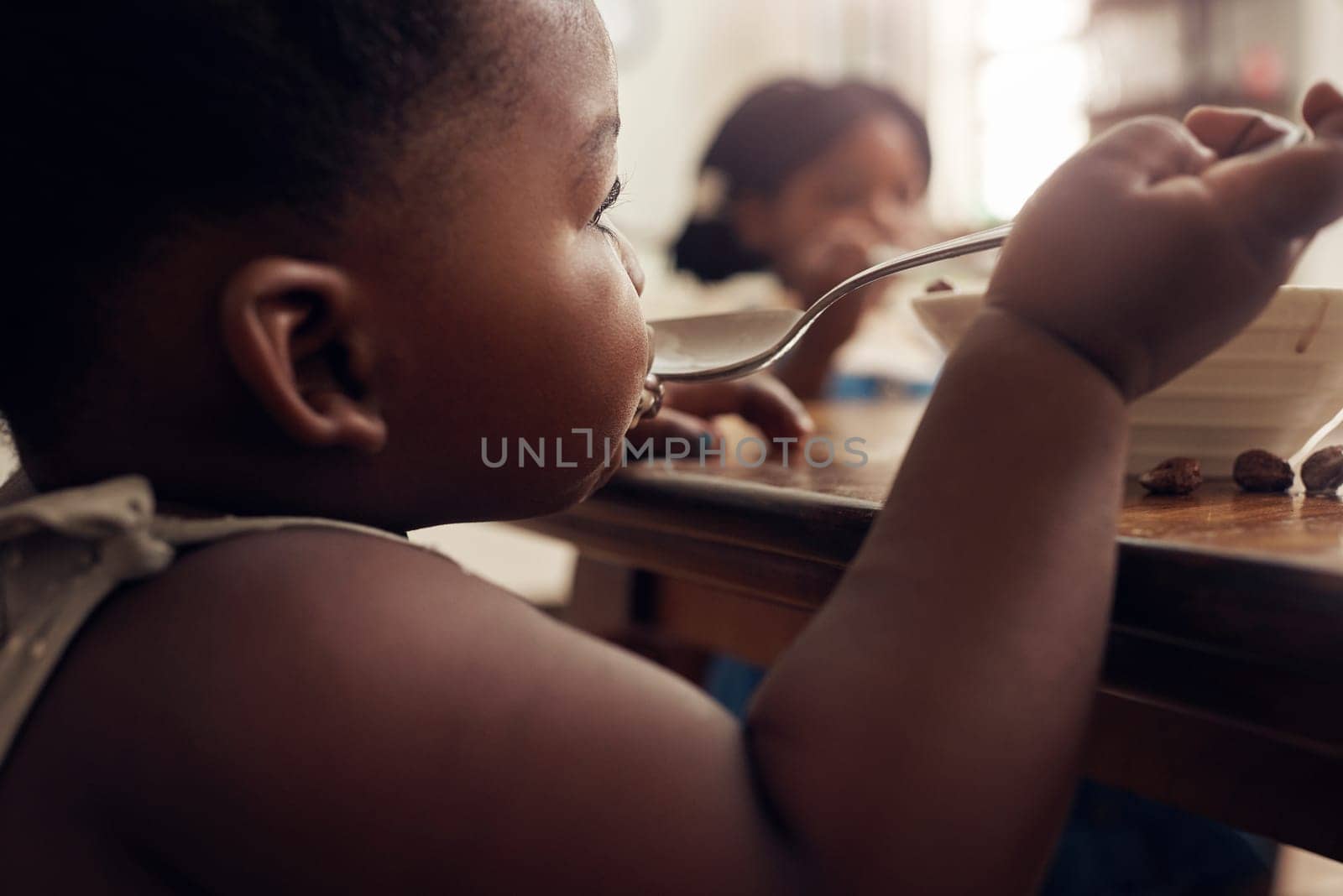 Black child, cereal spoon and eating baby in a home kitchen with food and bowl at breakfast. African girl, nutrition and youth in a house with hungry kid relax with healthy snack and kids at morning by YuriArcurs