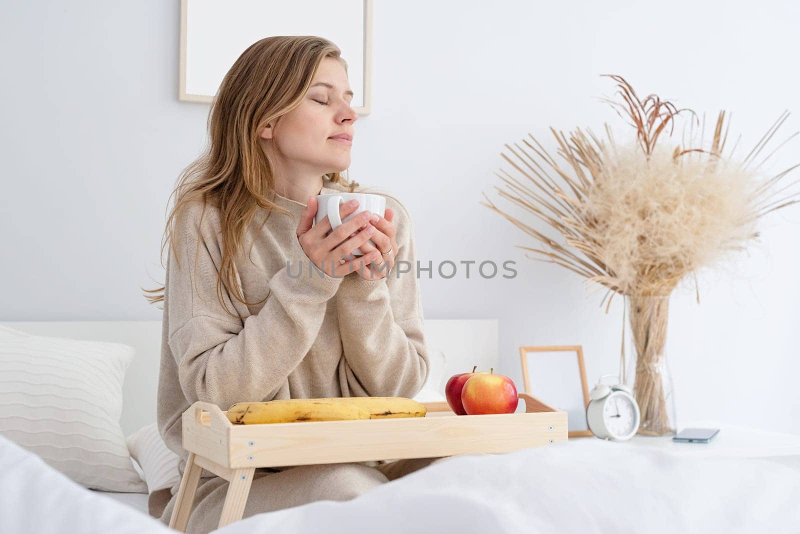 caucasian woman waking up in her bed in the morning. young millennial woman sitting on the bed in the morning drinking coffee, light and airy room