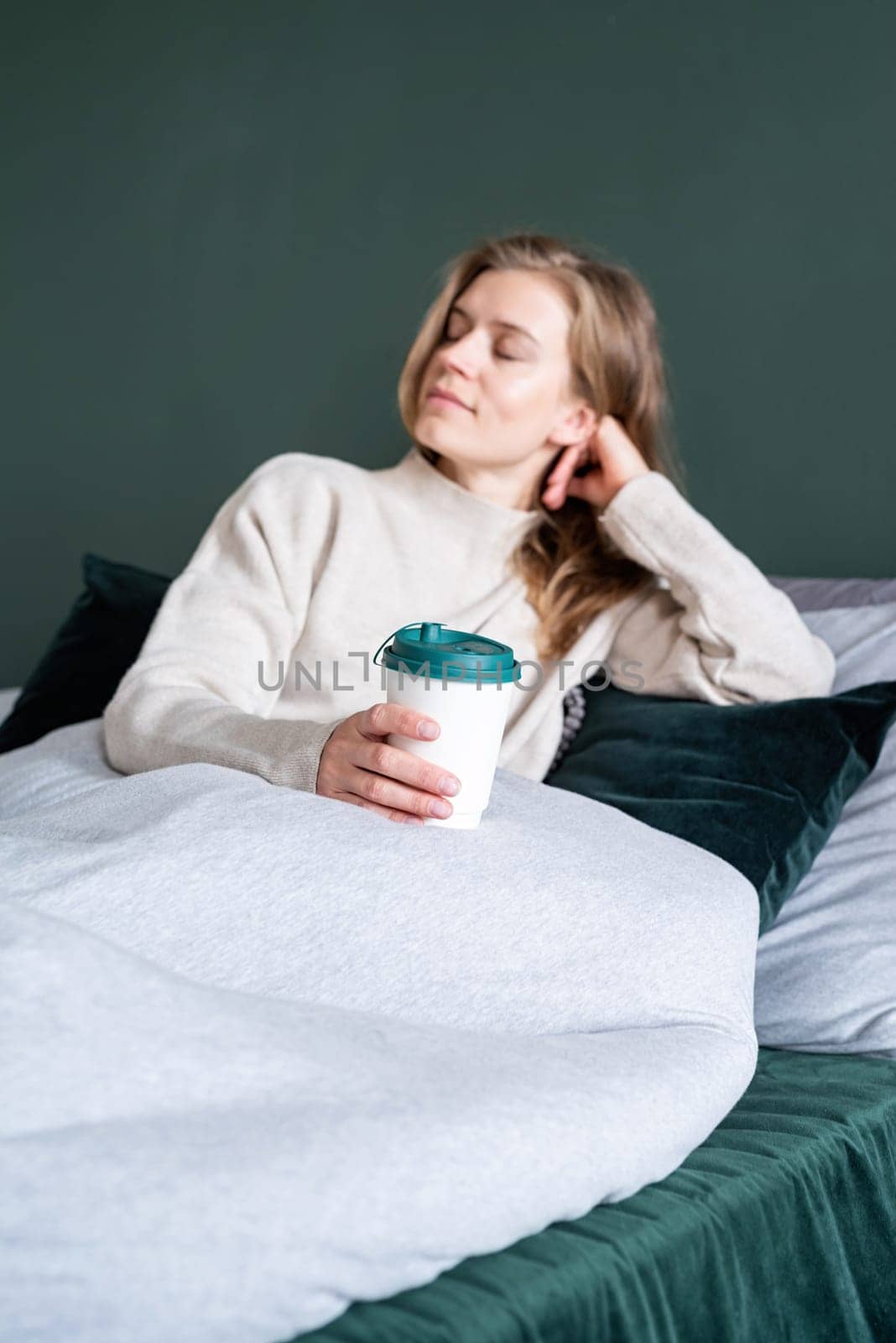 caucasian woman waking up in her bed in the morning. young millennial woman sitting on the bed in the morning drinking coffee from paper cup, mockup design