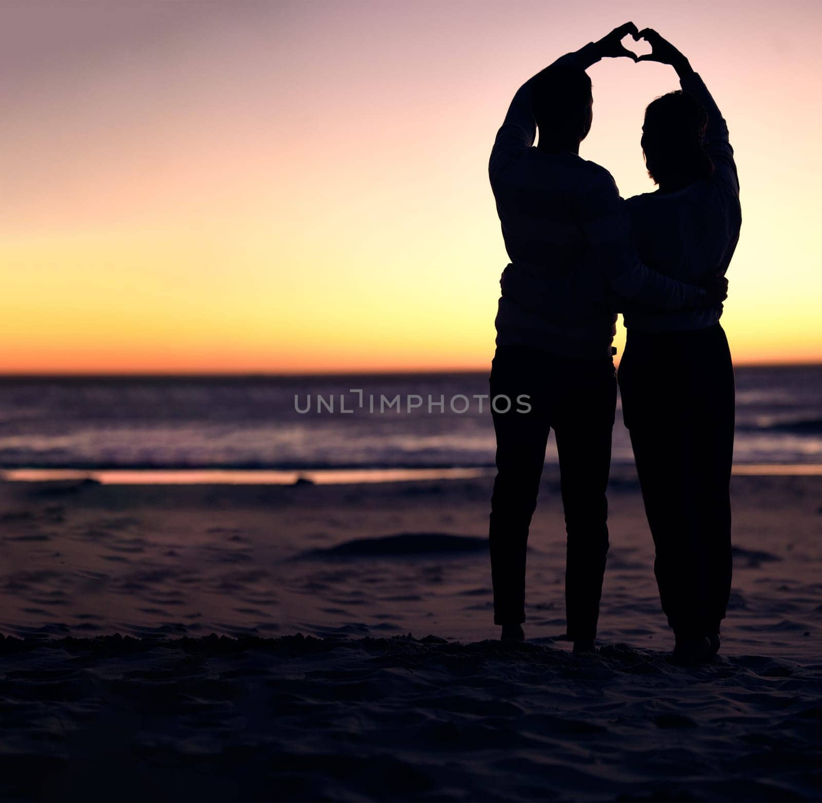 Couple, sunset silhouette and beach with heart sign hands, bonding and love on vacation for honeymoon. Man, woman and romantic hand signal by ocean with dusk sunshine for romance together in nature.