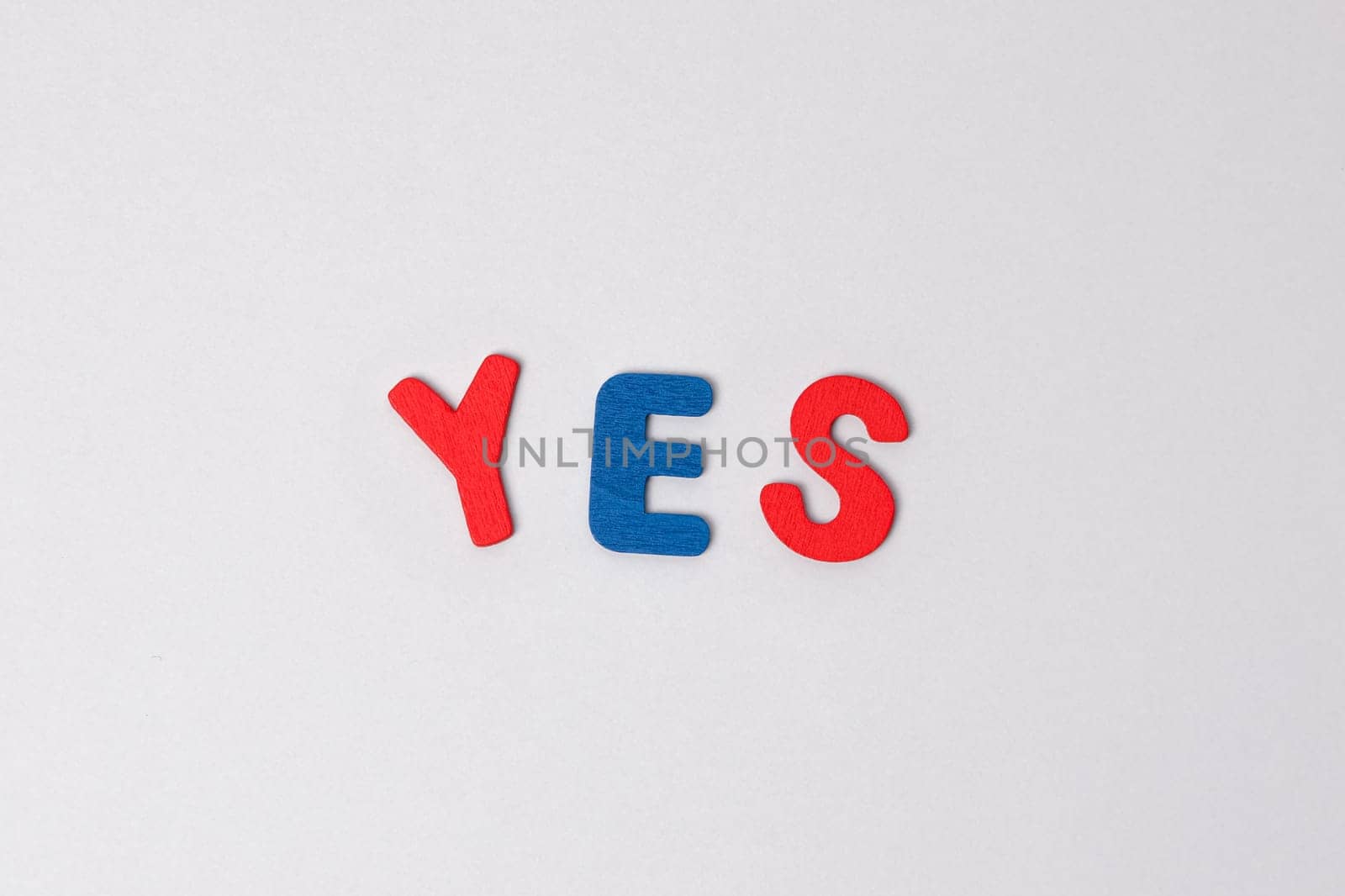 The word yes made of colored wooden letters on a light gray background. Blue and red letters form the word yes