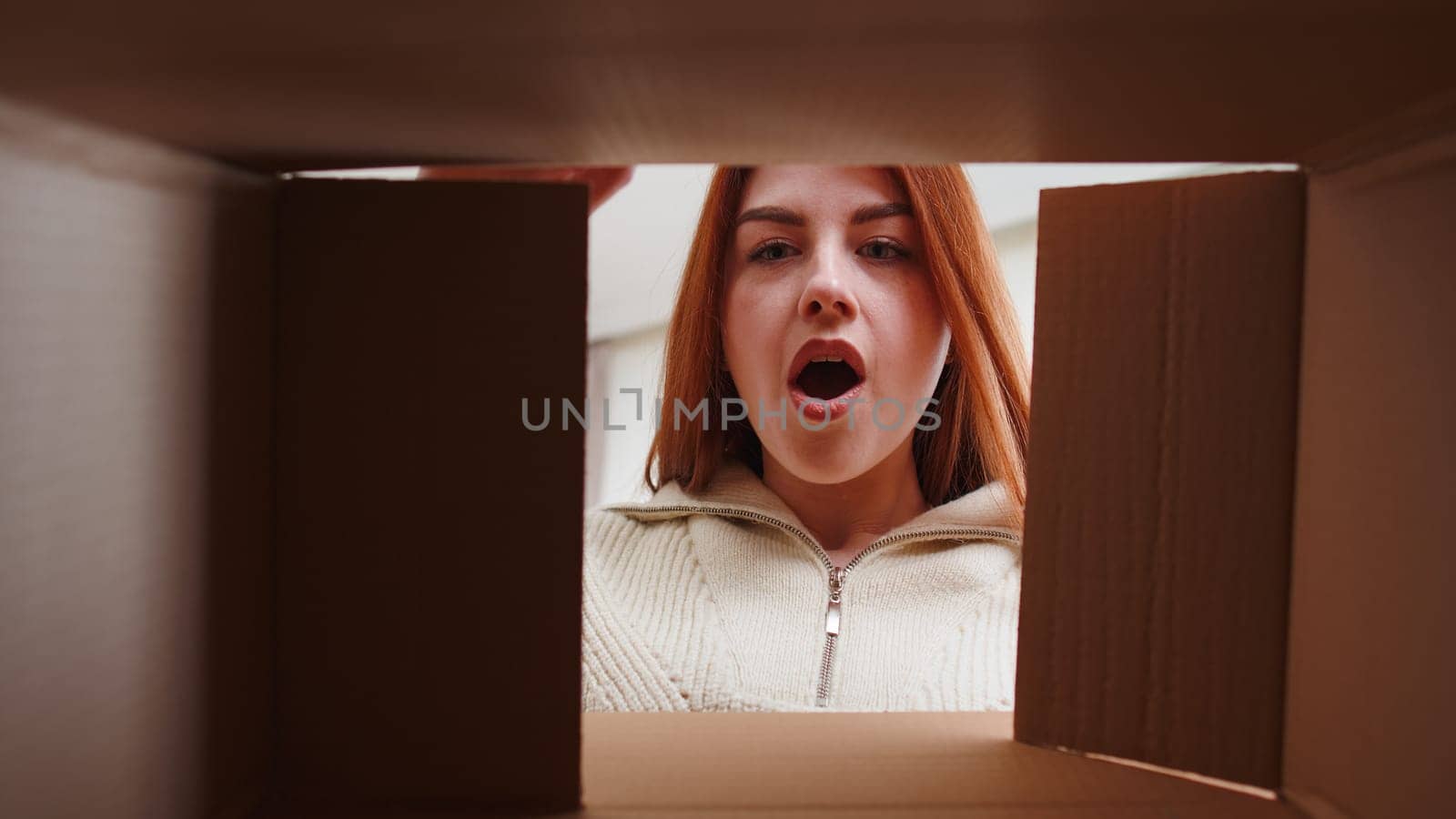 Inside view from box. Happy redhead woman unpacking delivery parcel at home. Smiling satisfied girl shopper online shop customer opening cardboard receiving purchase gift by fast postal shipping order