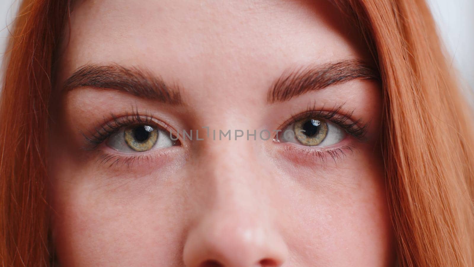 Extreme close-up macro portrait of smiling young woman freckles face. Redhead girl eyes, looking at camera. Green eyes of ginger lady. Portrait of teenager positive female opening wide her closed eyes