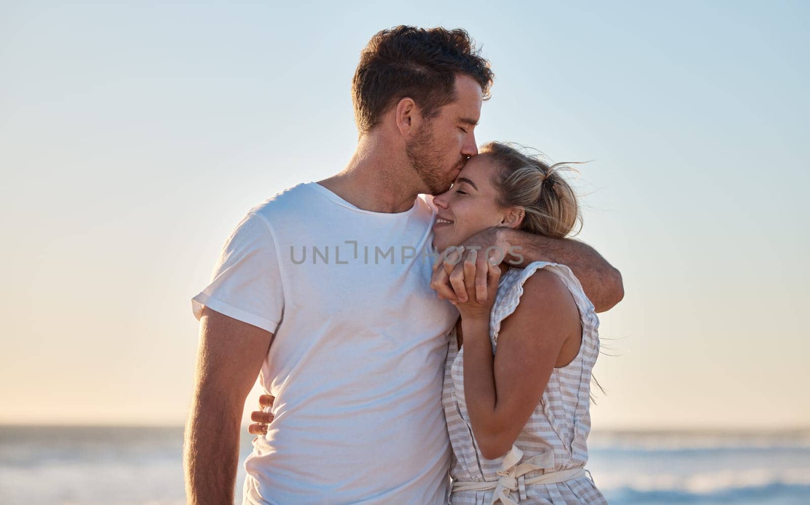 Love, summer and couple kiss at beach for intimacy, romance and loving relationship on honeymoon. Dating, affection and man and woman bonding and enjoy holiday, vacation and weekend together by ocean.