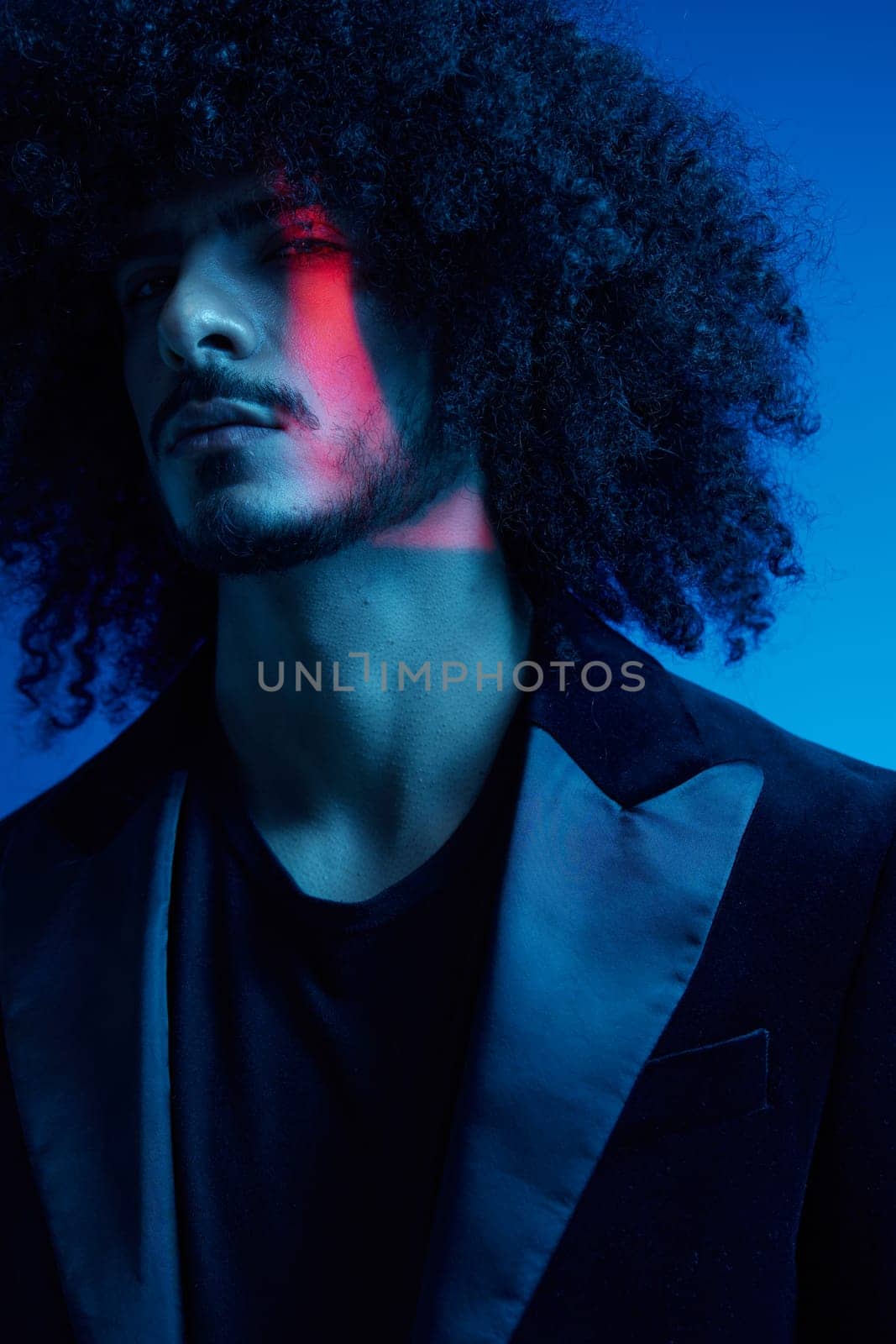 Fashion portrait of a man with curly hair on a blue background, multinational, colored light, trendy, modern concept. by SHOTPRIME