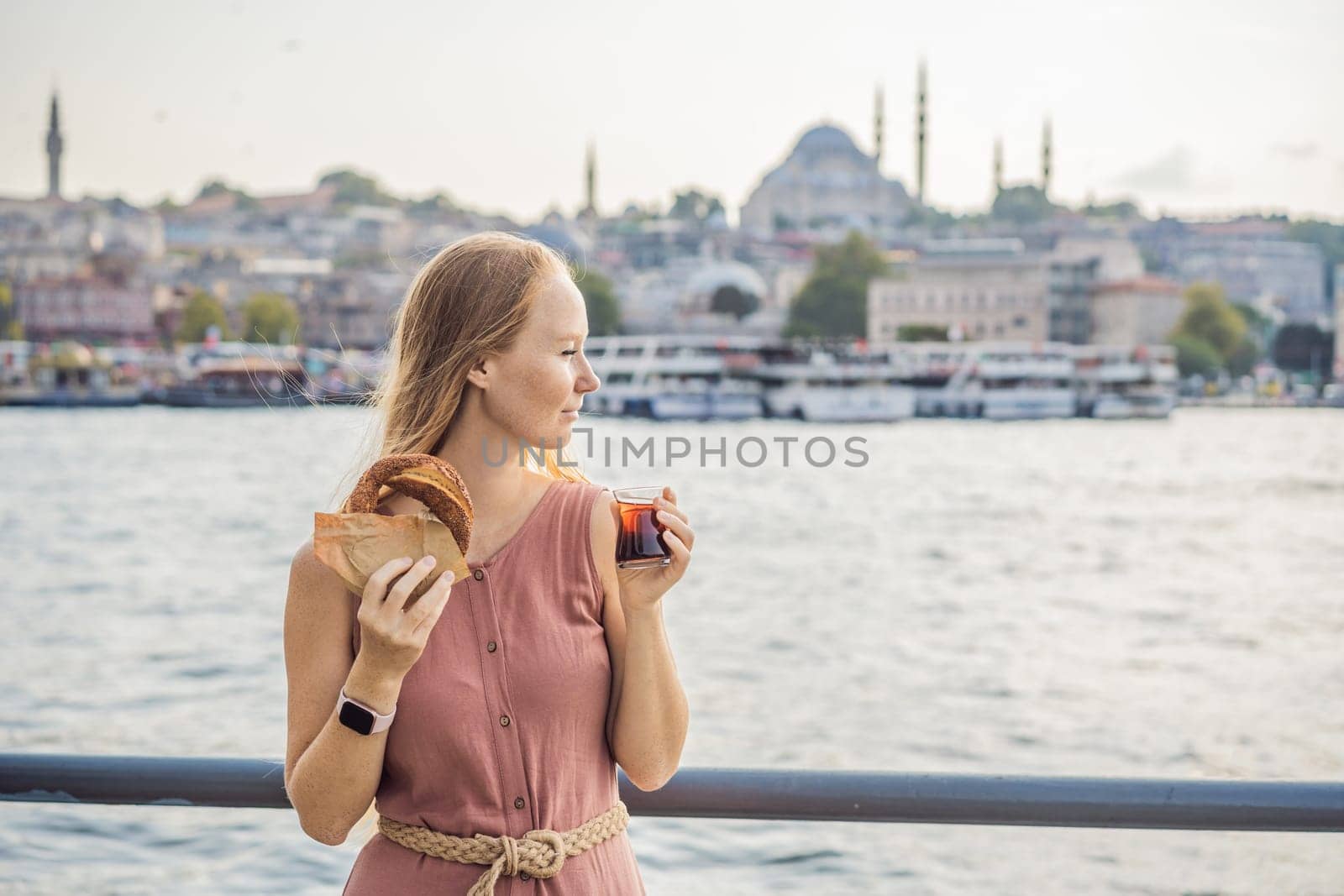 Woman in Istanbul having breakfast with Simit and a glass of Turkish tea. Glass of Turkish tea and bagel Simit against golden horn bay in Istanbul, Turkey. Turkiye.