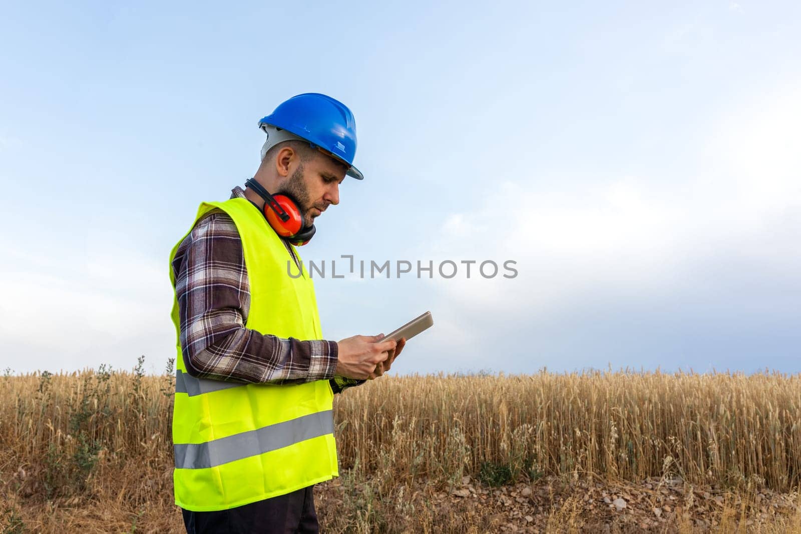 Side view of male maintenance worker wearing helmet and vest checking data on digital tablet. Copy space. by Hoverstock