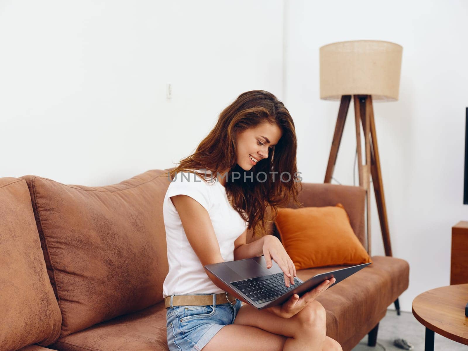 Woman freelancer sitting on the couch with a laptop beautiful smile , modern stylish interior Scandinavian lifestyle, copy space. High quality photo