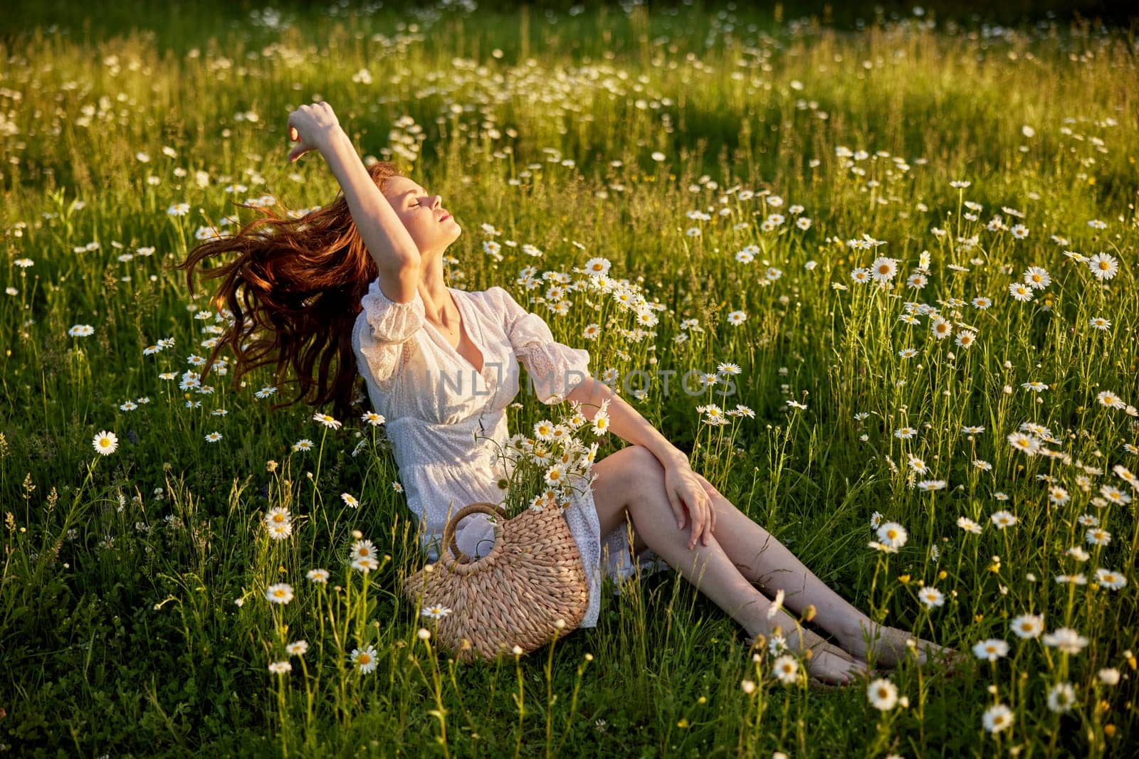 a beautiful woman in a light dress sits in a field in chamomile flowers. High quality photo