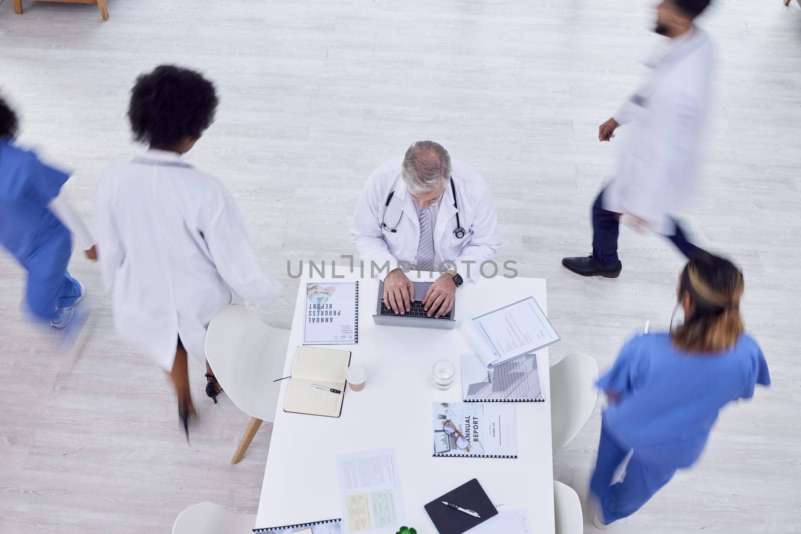 Doctor, man and laptop in busy hospital for medicine research, surgery schedule management or medical life insurance. Top view, healthcare worker and surgeon on technology with motion blur coworkers.