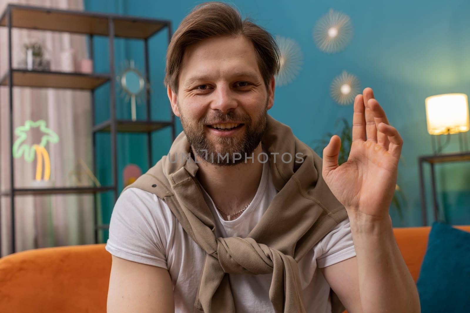 POV of Caucasian man looking at camera, making video webcam conference call with friends or family, enjoying pleasant conversation at home room apartment. Guy sitting on sofa laughing, waving hello