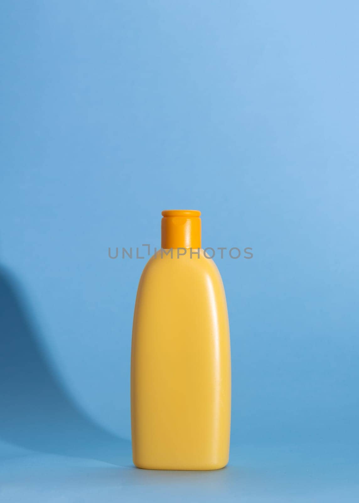 Mock up of a yellow bottle with children's cosmetics on a blue background. Hard shadows, copy space by Ri6ka