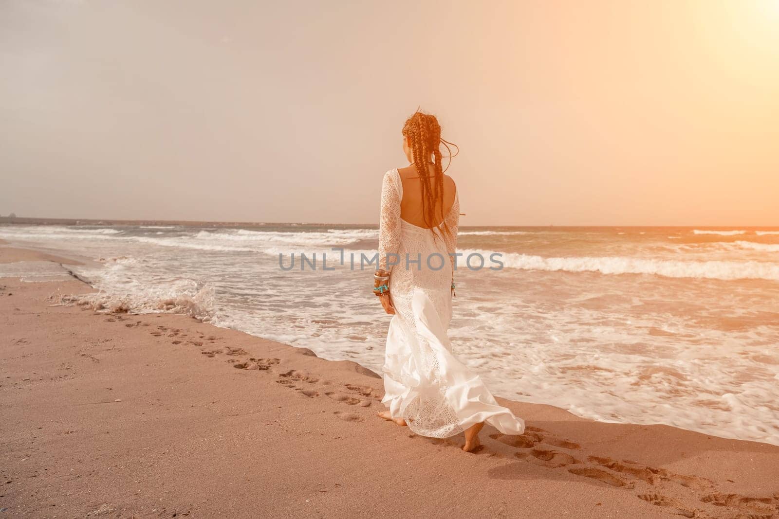 woman sea white dress. Model in boho style in a white long dress and silver jewelry on the beach. Her hair is braided, and there are many bracelets on her arms. by Matiunina