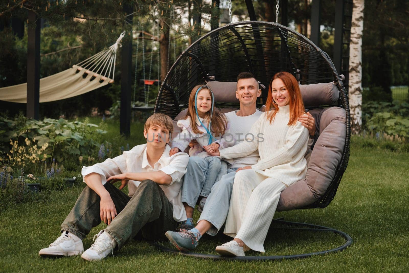 A happy family is sitting in a hammock on the lawn near the house by Lobachad