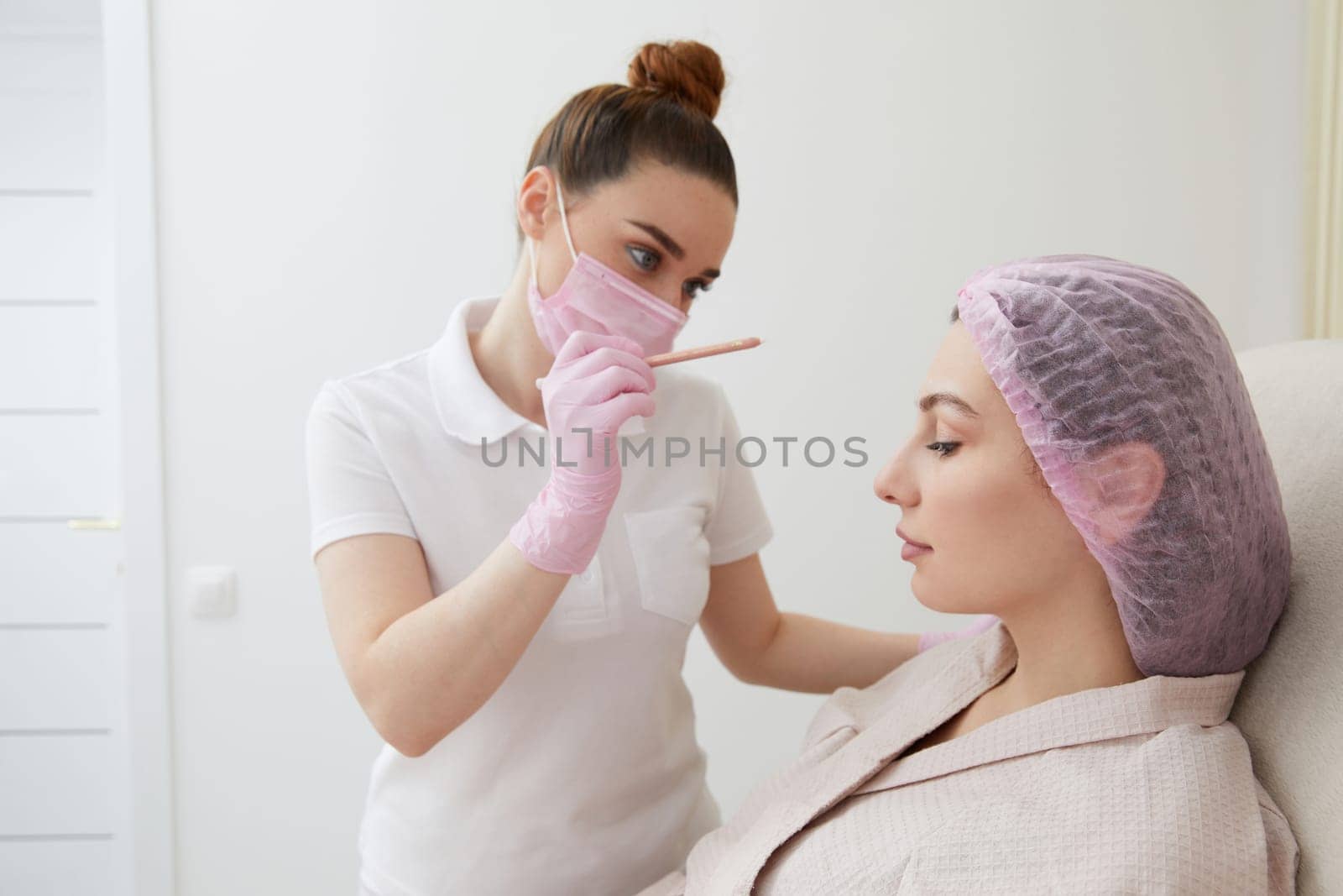 Cosmetologist drawing mark on client face to prepare for a rejuvenation treatment