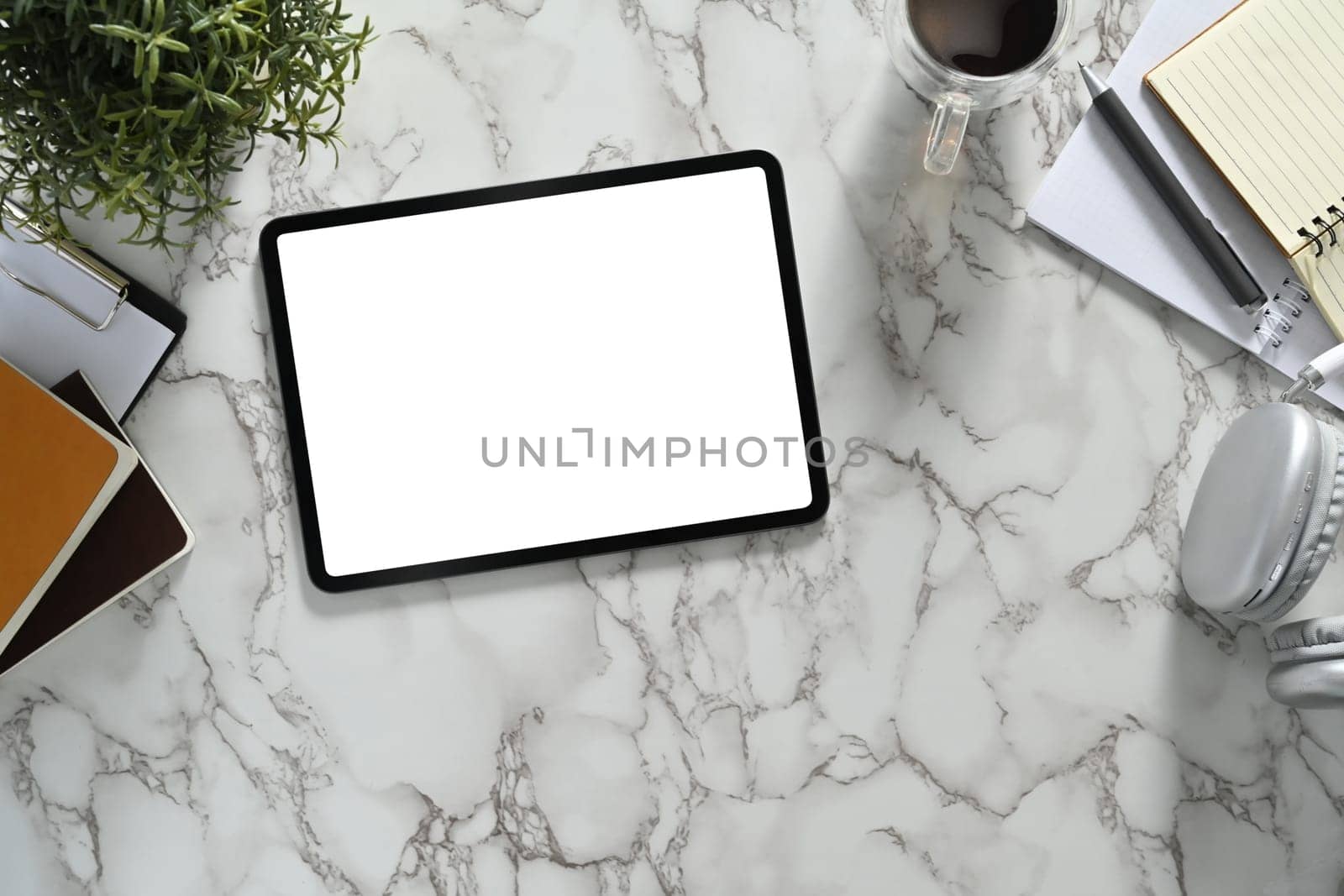 Top view of digital tablet with white empty screen, headphone and coffee cup on marble background.