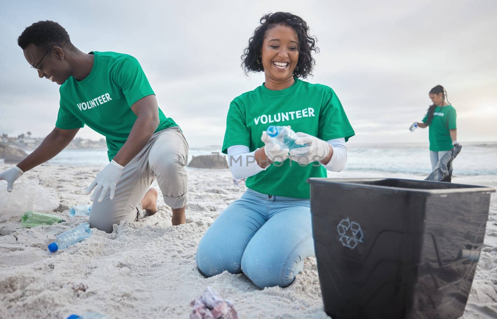 Volunteer group, beach clean and recycling plastic bottle for community service, pollution and earth day. Black woman and man ngo team cleaning sand for climate change, nature and helping environment.