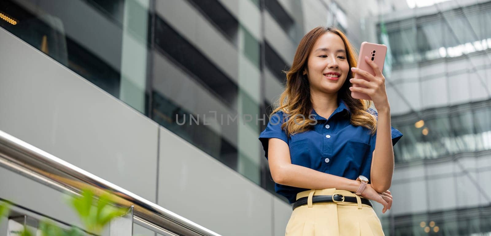 Young woman walking in the city with blue shirt and using smartphone. Girl using smart phone app for messaging, browsing and shopping.