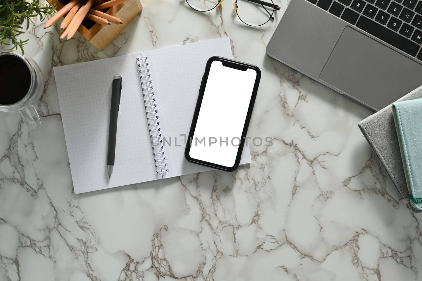 Smartphone with blank screen, laptop notepad and glasses on marble table. Flat lay, Top view.