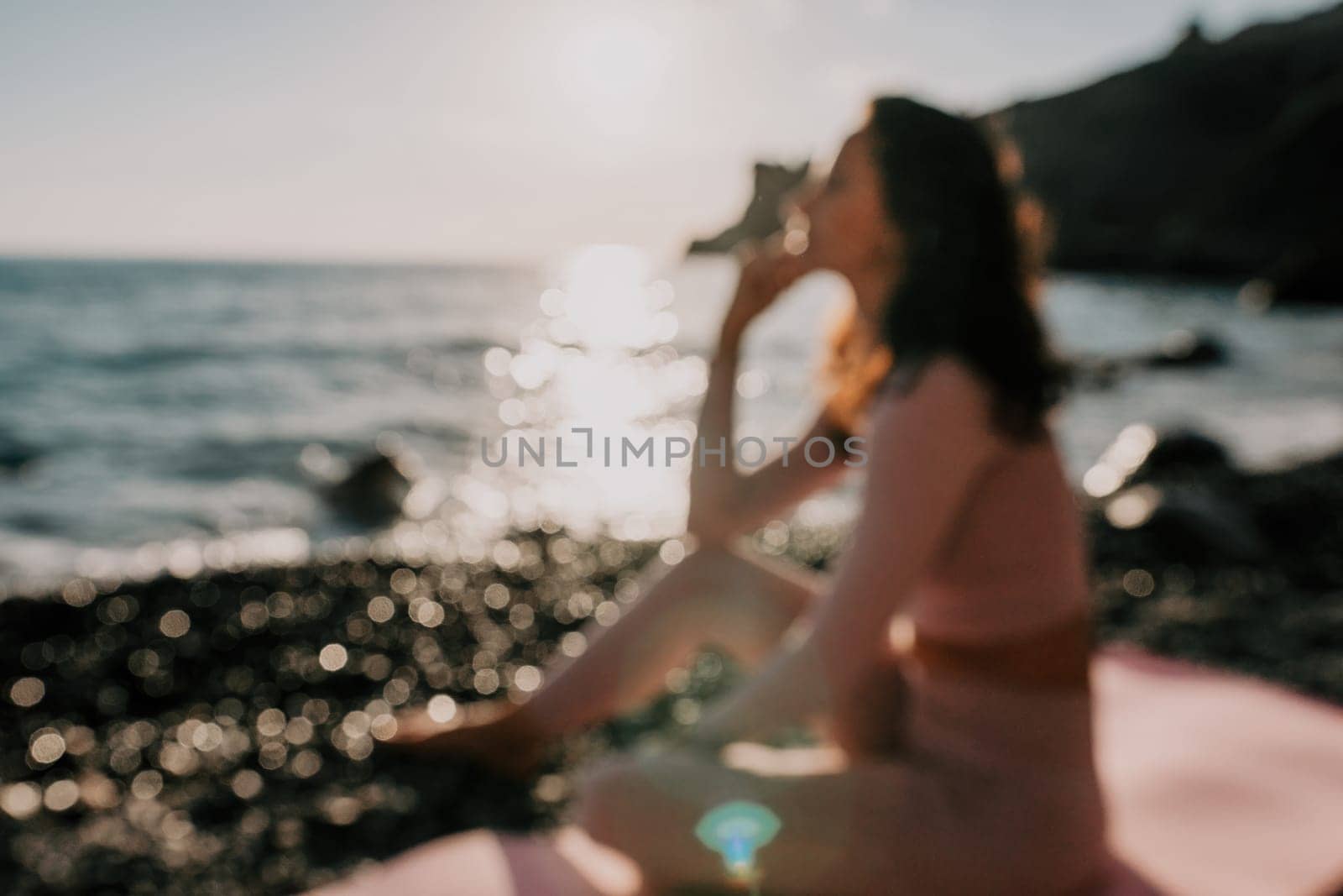 Young woman with black hair, fitness instructor in pink sports leggings and tops, doing pilates on yoga mat with magic pilates ring by the sea on the beach. Female fitness daily yoga concept