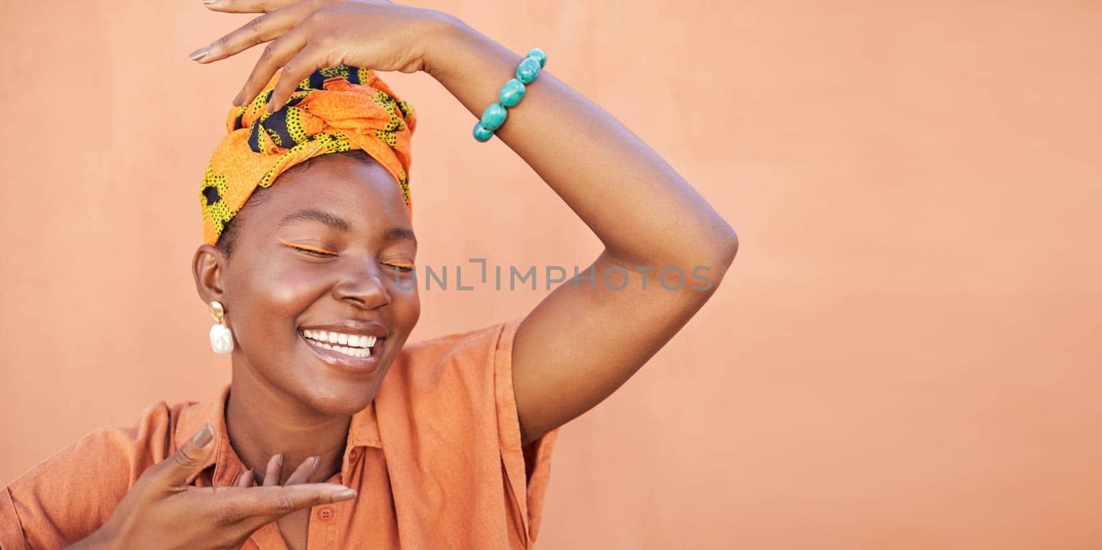 African, fashion and face of black woman on orange wall background with natural beauty, makeup and smile. Culture, hands and girl in Nigeria with designer jewelry, exotic cosmetics and head scarf.