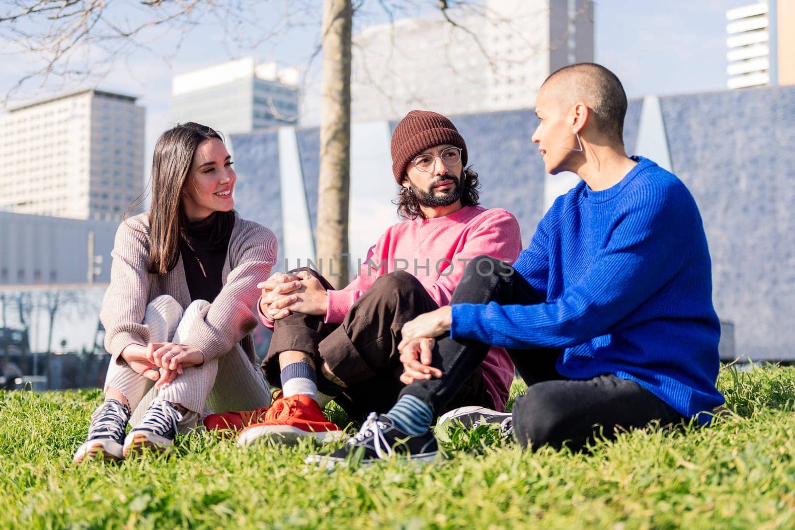 three young friends enjoying conversation in a sunny day at the city park, concept of friendship and urban lifestyle