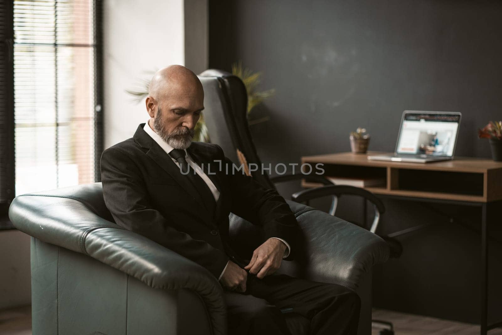 sad and contemplative old mature senior man sits in dignified leather chair. Dressed in suit, exudes sense of professionalism and experience, as he reflects on thoughts in solitude of room. High quality photo