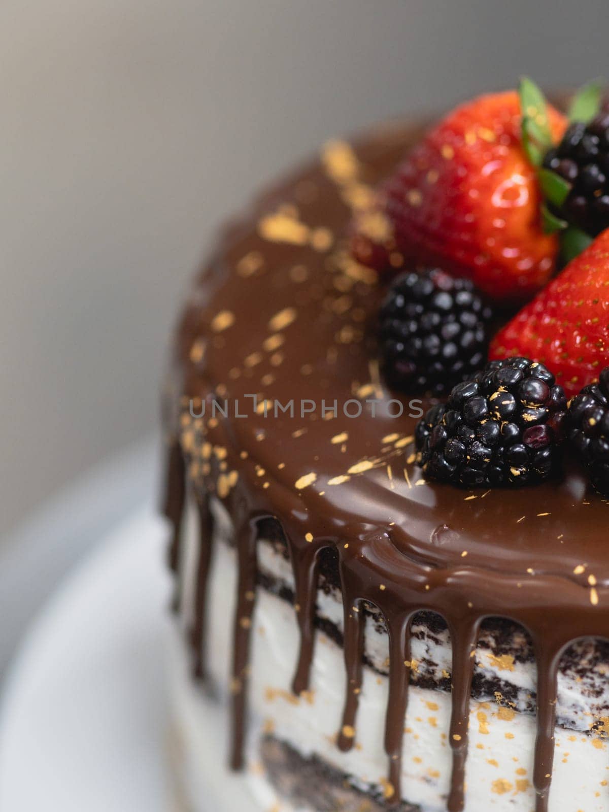 pastry chef preparing a chocolate frosted dripped icing cup cake with sweet fruit topping and golden brush strokes