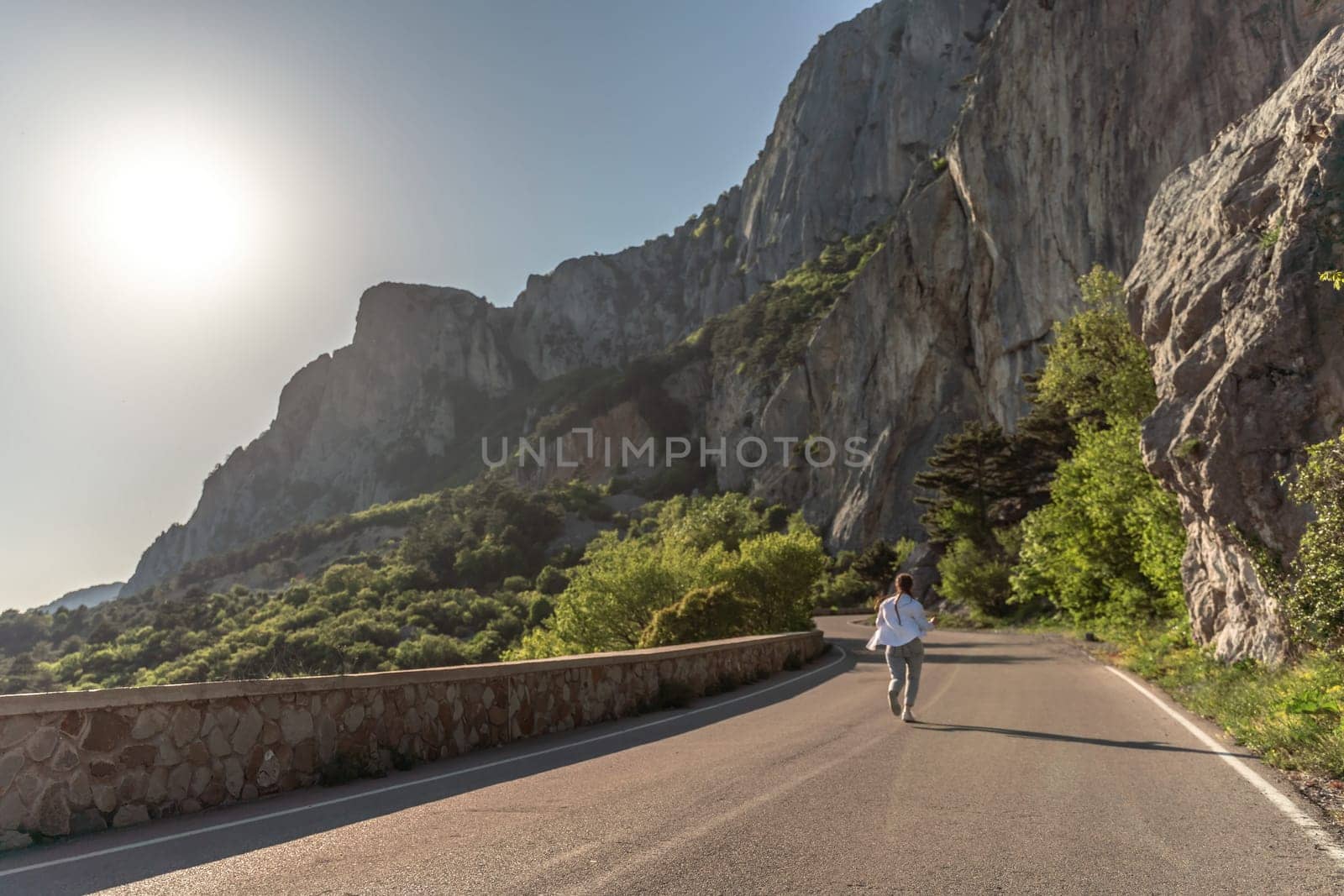 A woman runs along an asphalt road in the middle of a mountainou by Matiunina