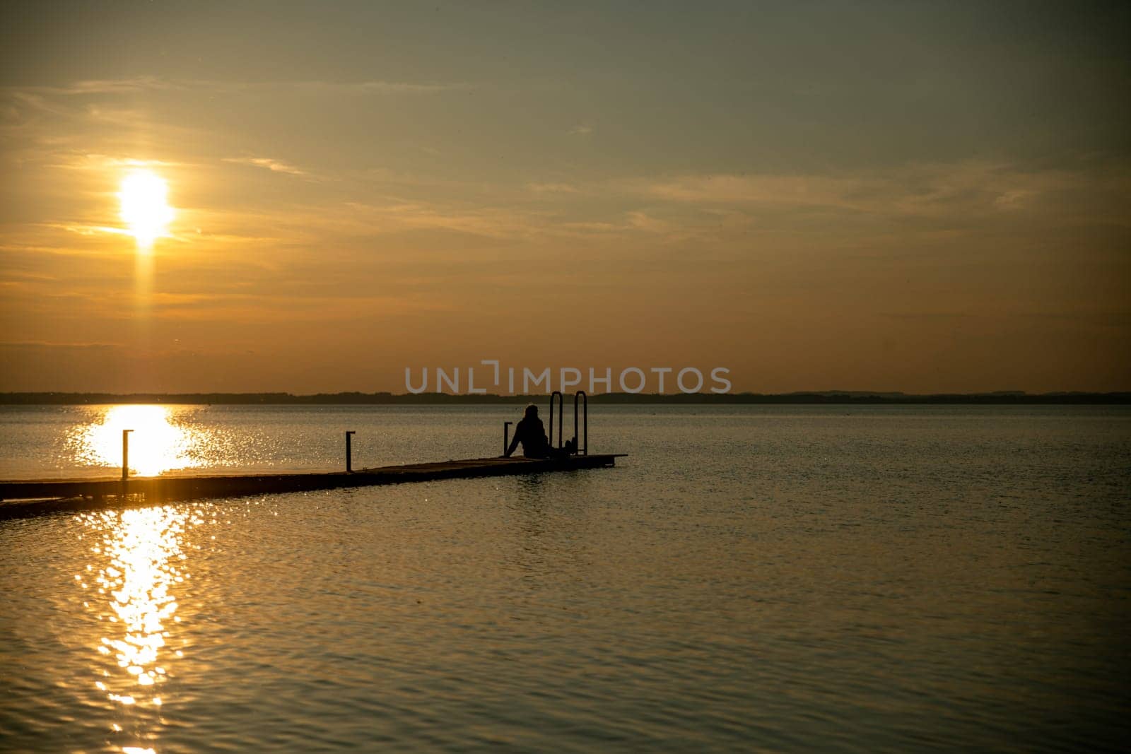 the silhouette of a woman sitting on a wooden jetty by the water by compuinfoto