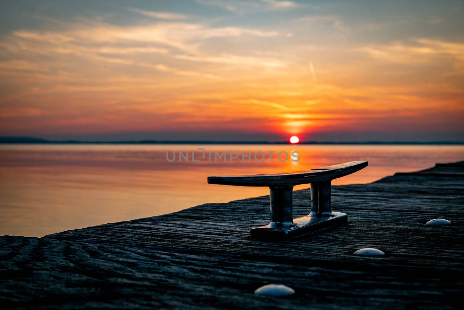 a steel mooring rope on the quay during sunset with the sun sinking into the water of the chiemsee in the background with orange and red skies