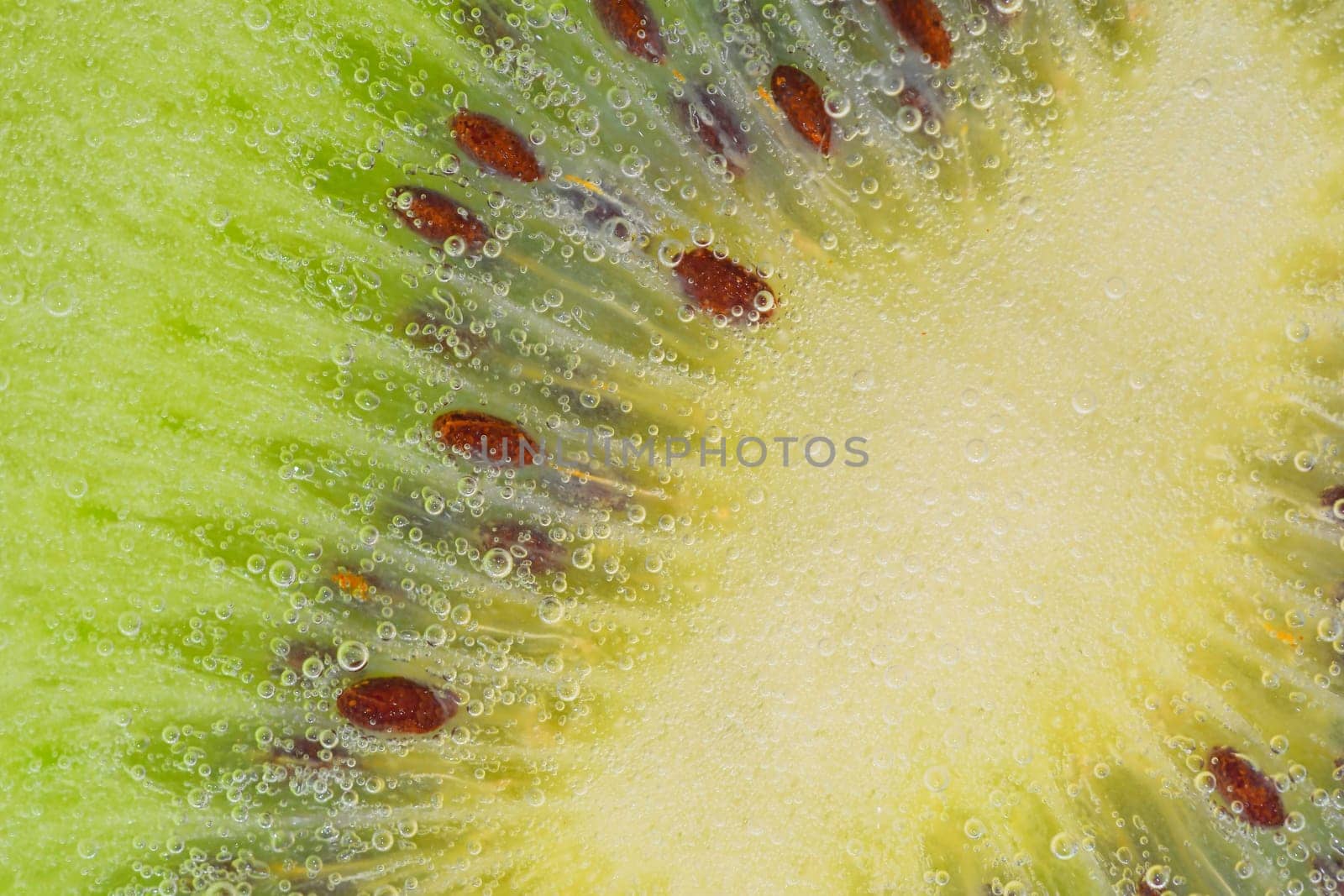 Close-up of a kiwi fruit slice in liquid with bubbles. Slice of ripe kiwi fruit in water. Close-up of fresh kiwi slice covered by bubbles. Macro horizontal image