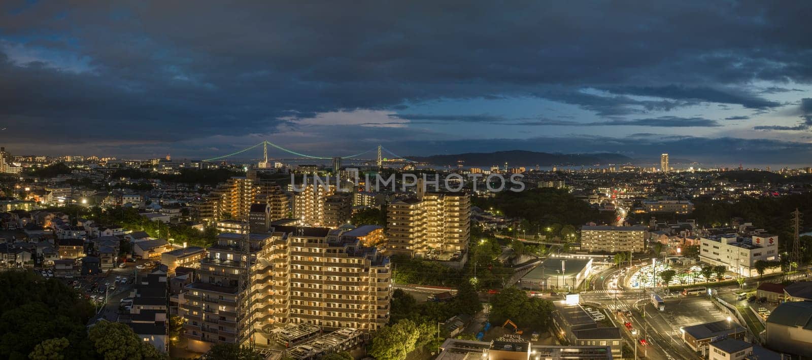 Lights from apartments and intersection in city with distant bridge at night by Osaze