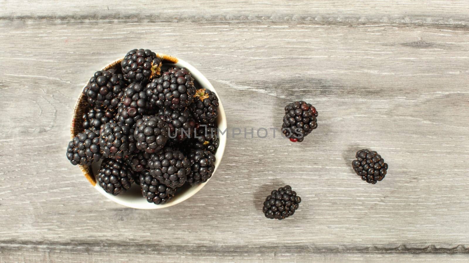 Top down view, small bowl with blueberries some of them spilled on desk.