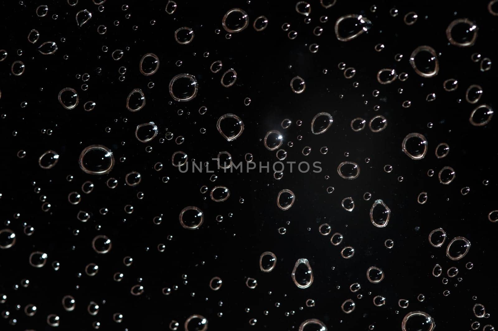 Detail photo - rain water drops behind glass look like bubbles in black liquid. Abstract wet background.
