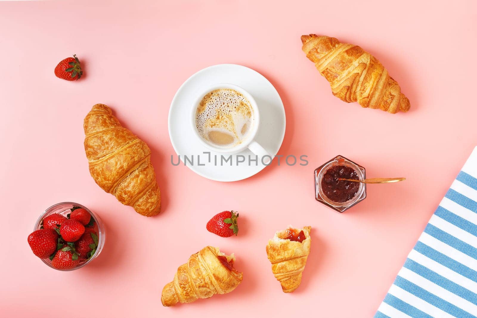 Delicious breakfast with fresh croissants, coffee, berry jam and fresh berries on a pink background.