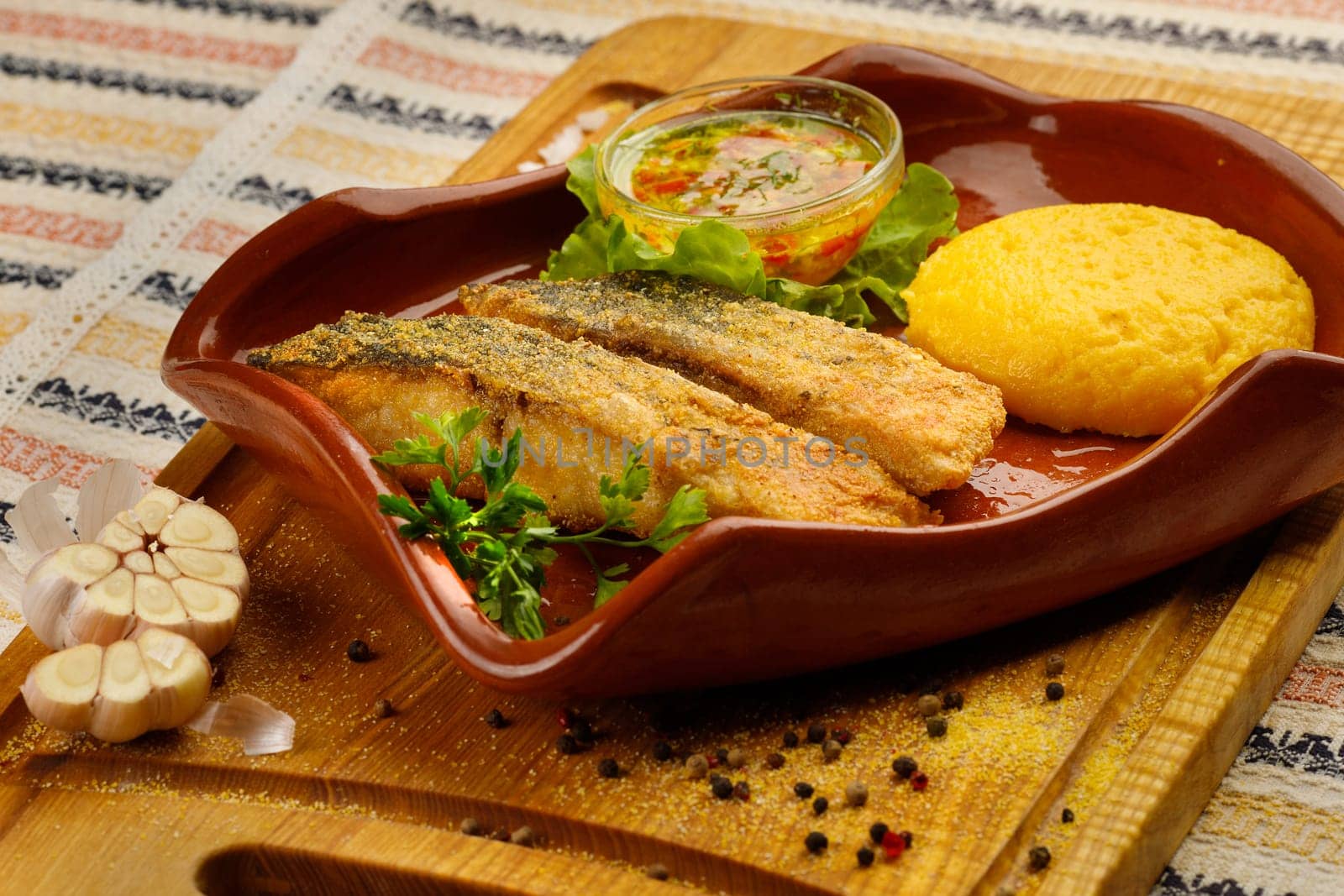 Whole fried fish in a red plate served with mamaliga and garlic souce