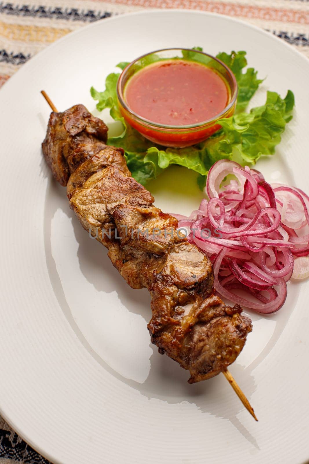 Grilled pork kebab with red onion and chilly souce on a white plate