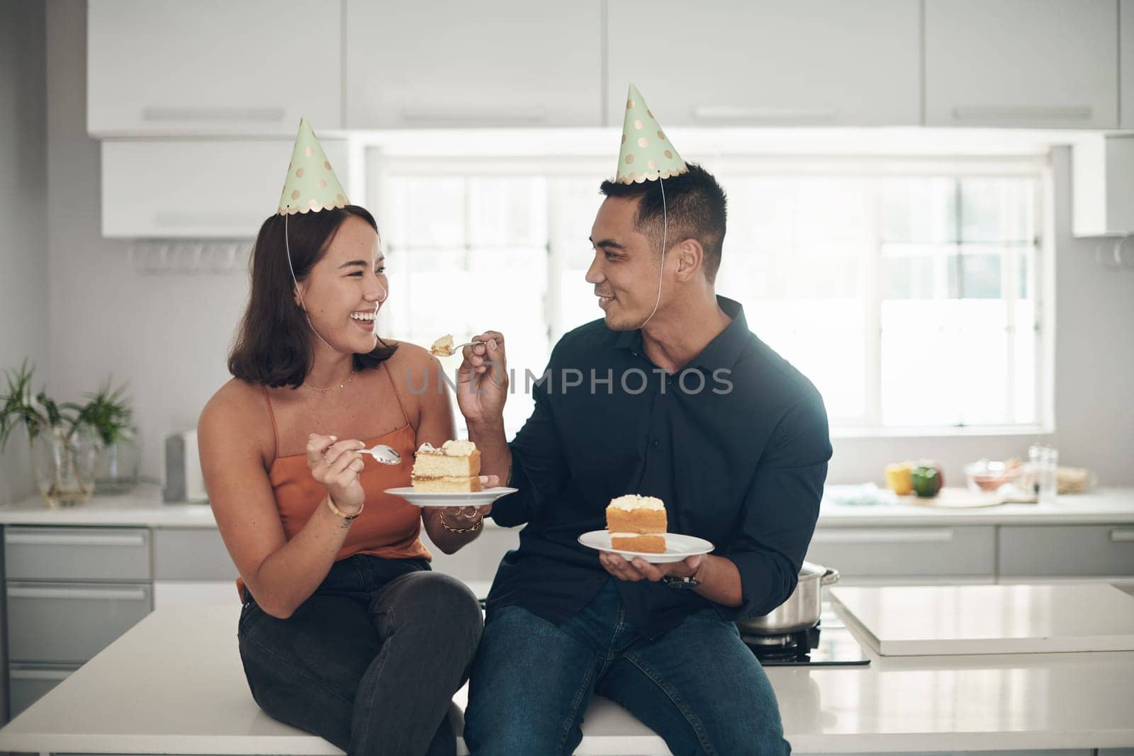 Birthday cake, celebration and couple in a kitchen, happy and relax while bonding in their home, smile and laugh. Party, people and man with woman on counter for eating, fun and celebrating in Japan.