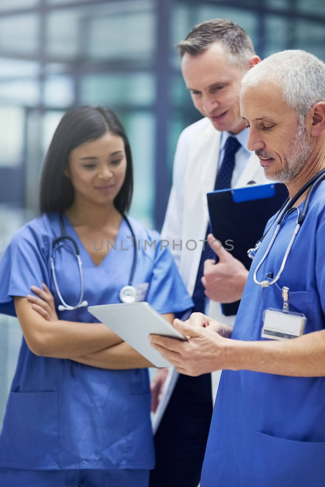 Shot of a group of doctors talking together over a digital tablet while standing in a hospital.